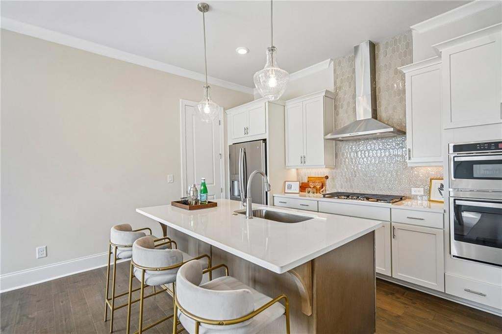 Contemporary kitchen featuring a large island with sink, white shaker cabinetry, stainless steel appliances, and a unique tiled backsplash