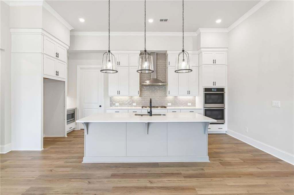 Modern kitchen featuring a large central island with a solid surface countertop, white shaker cabinetry, stainless steel double ovens, and wood-finish flooring