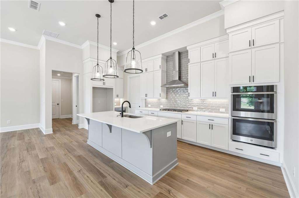 Kitchen featuring an expansive center island with seating, pendant lighting, stainless steel double ovens, and a tile backsplash