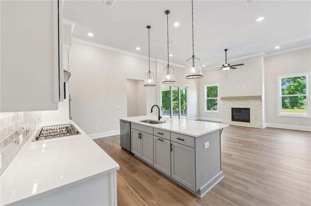 Open-concept living space with wood-finish flooring, a contemporary fireplace with stone surround, a kitchen island with pendant lighting, a gas cooktop, and sliding glass doors