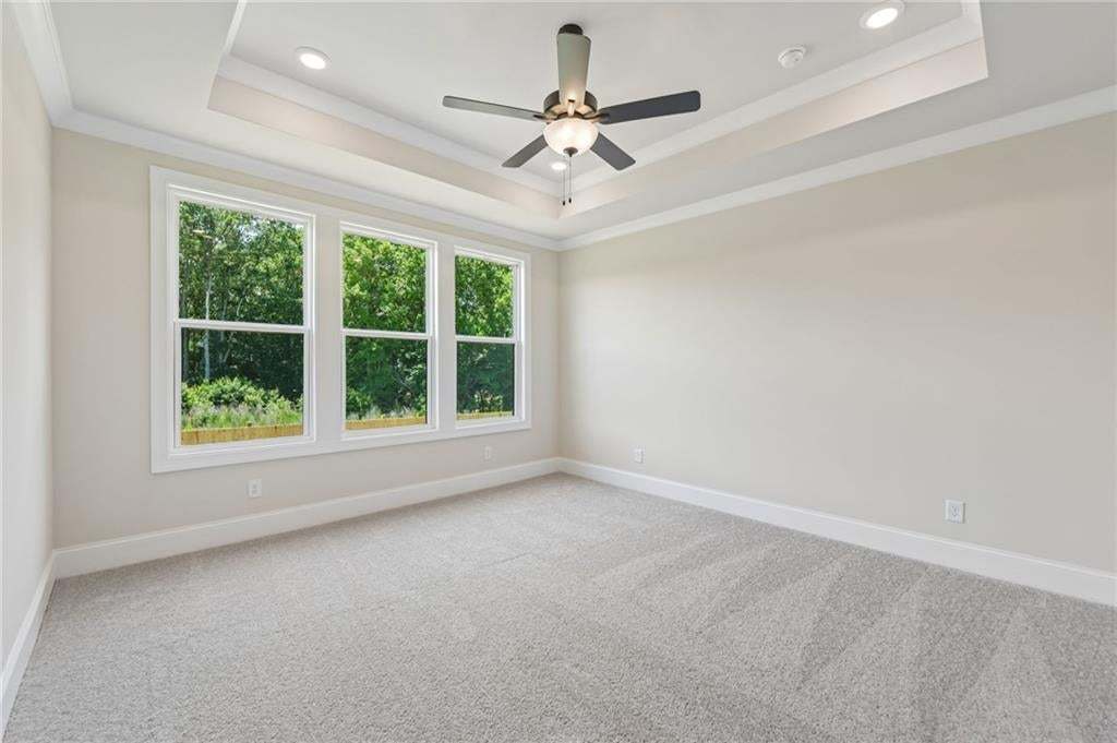 Tray ceiling with recessed lighting, ceiling fan, triple windows, and light grey carpet flooring