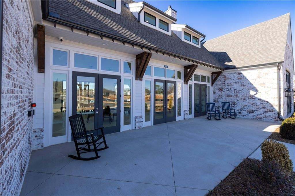 Whitewashed brick exterior featuring a covered concrete patio, multi-pane glass double doors, decorative wood corbels, and shingled roofline