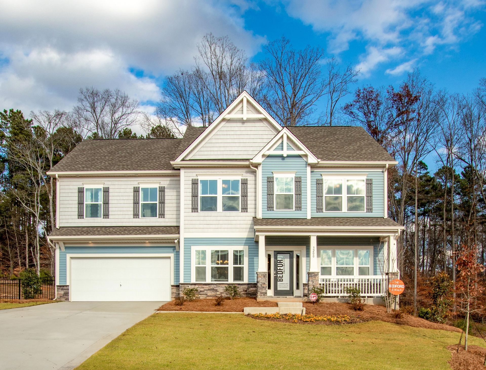 a large white and blue house with a garage and a porch surrounded by trees .
