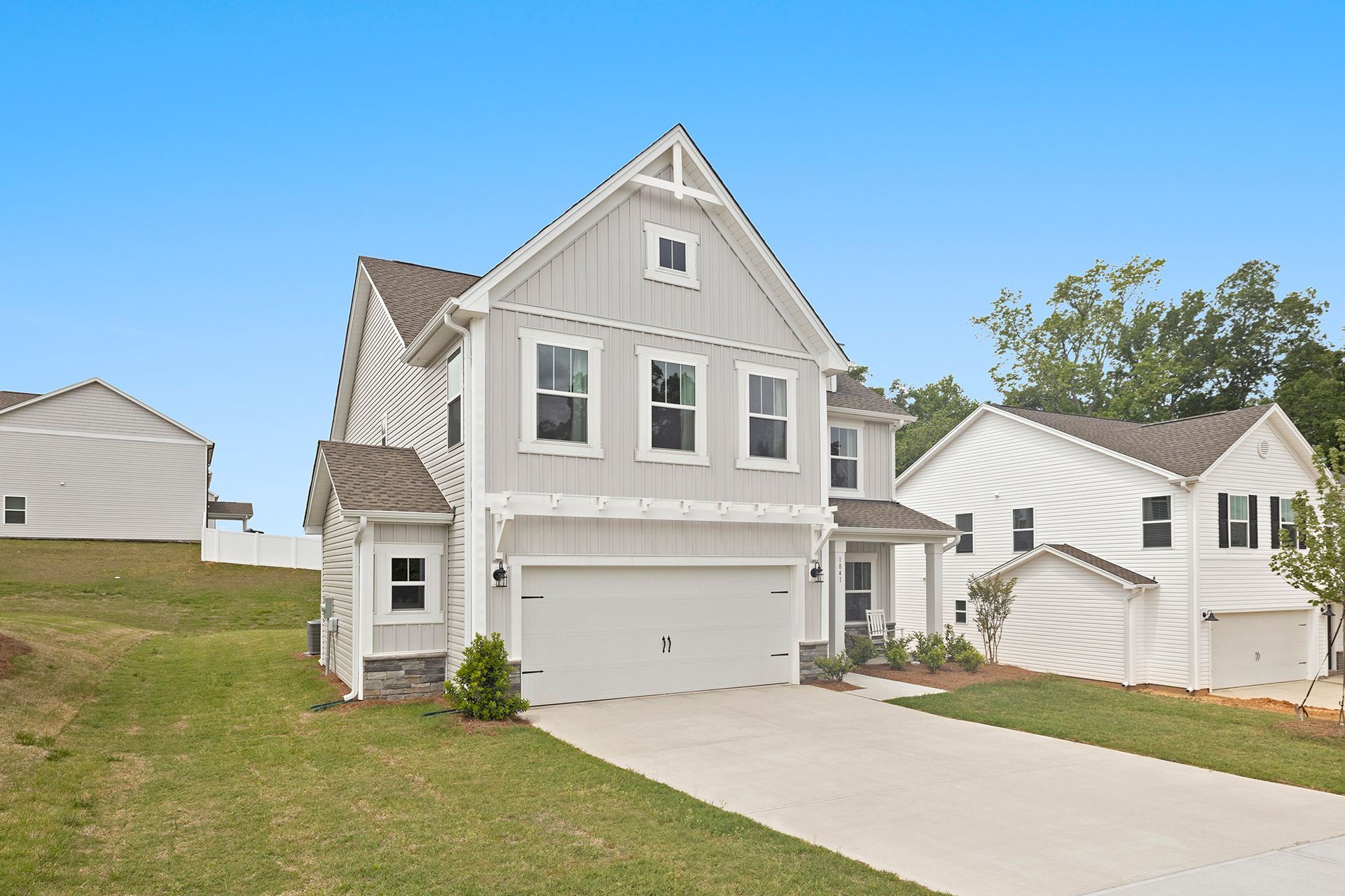 A white house with a large garage is sitting on top of a grassy hill.