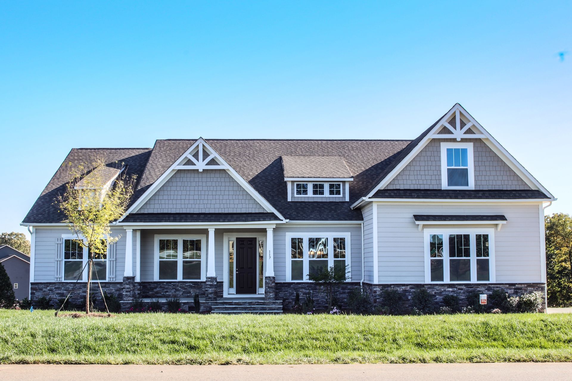 A large white house with a gray roof is sitting on top of a lush green field.