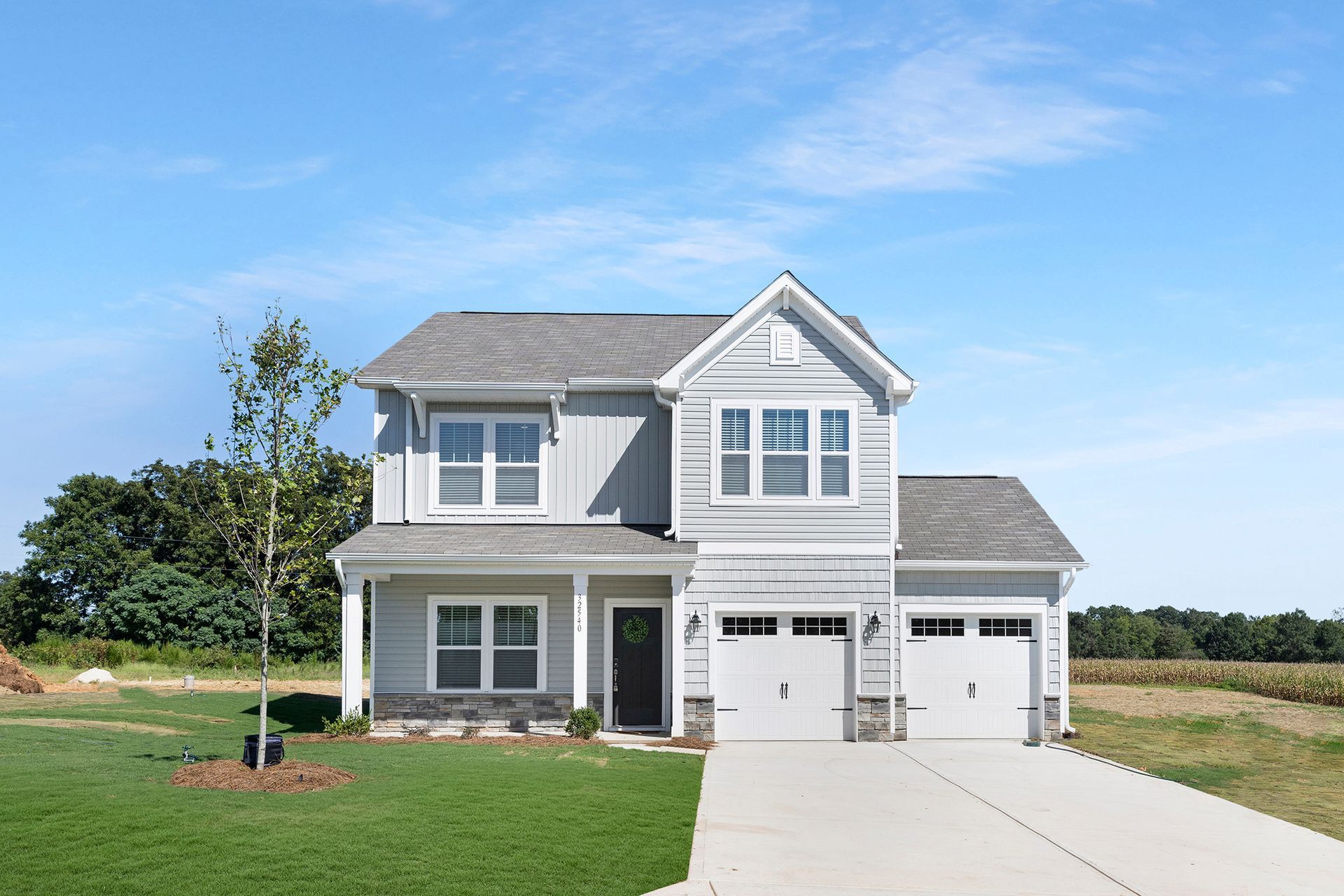 A white house with a gray roof is sitting on top of a lush green field.