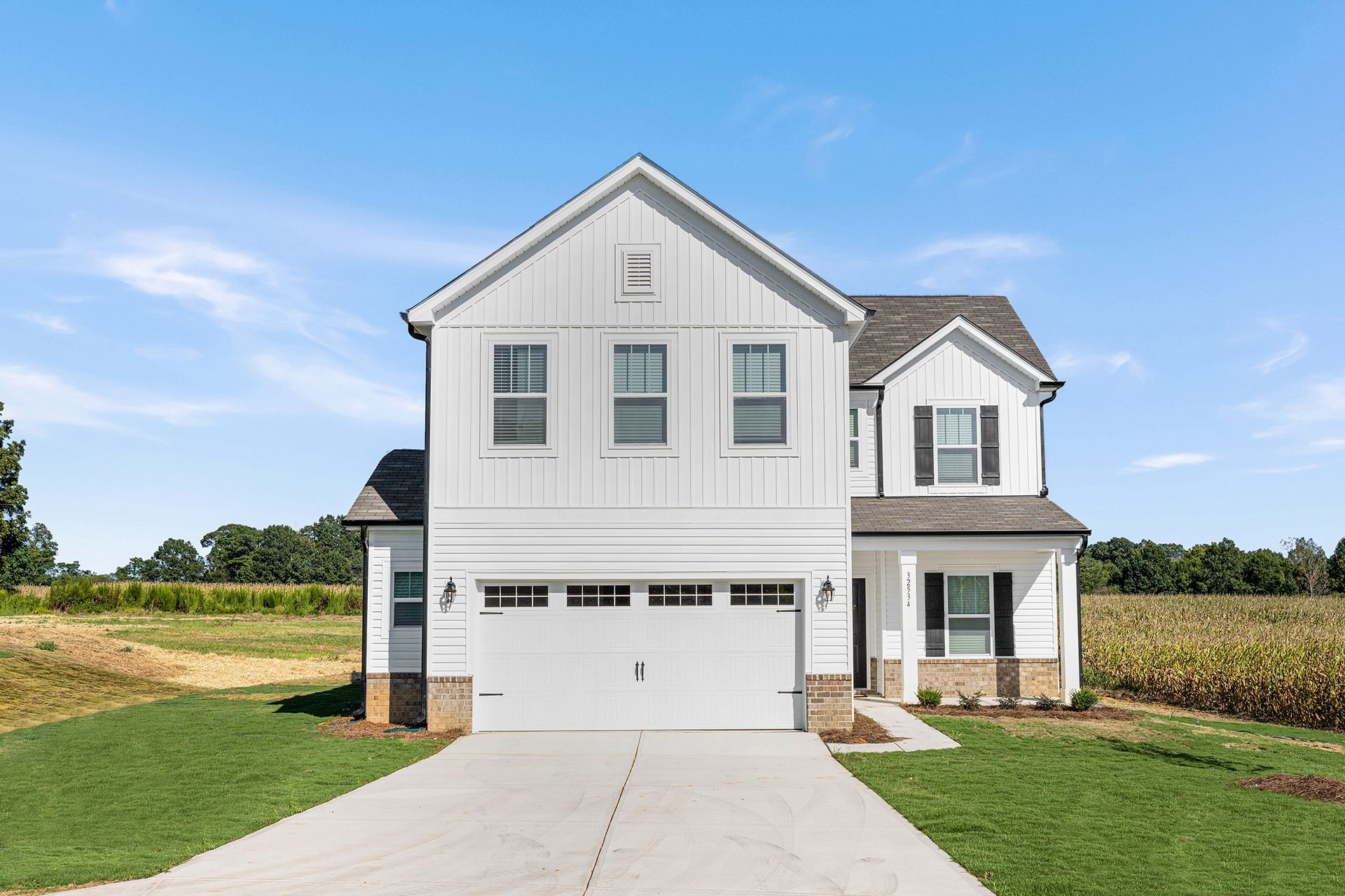 A white house with a garage and a driveway is sitting on top of a lush green field.