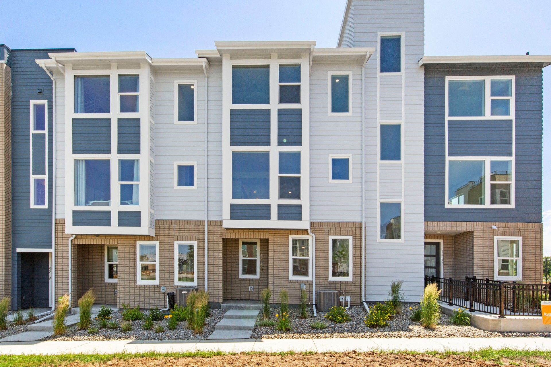 Modern Townhome with Spacious Windows at Antora, Dillon Pointe:Experience refined living at Antora, Dillon Pointe with sleek siding, expansive windows, and brick accents.