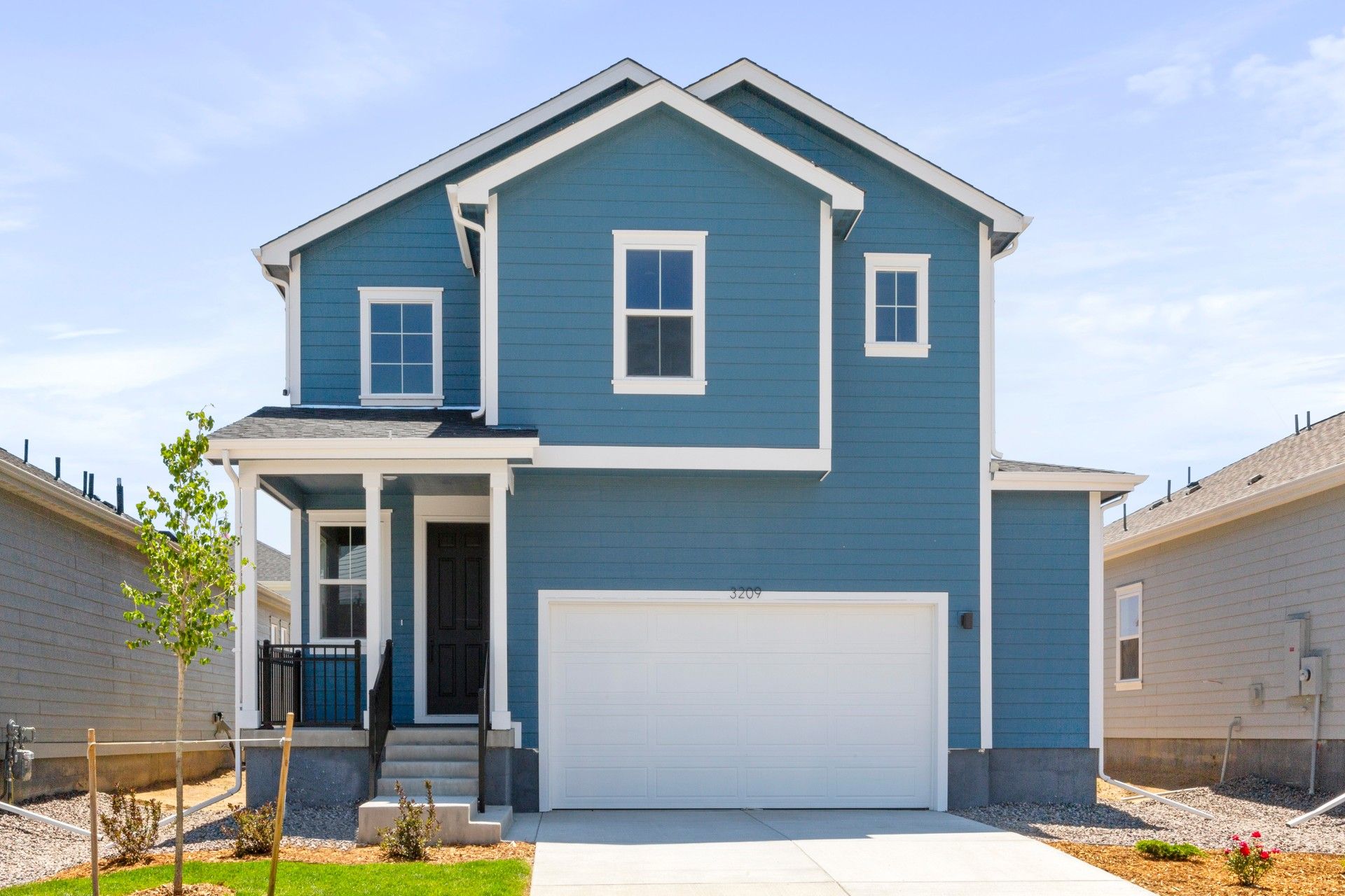 Blue Two-Story Home with Garage and Porch in Residential Area:Elegant blue façade with gabled roof and white trim. Spacious garage. Perfect spot in a serene neighborhood.