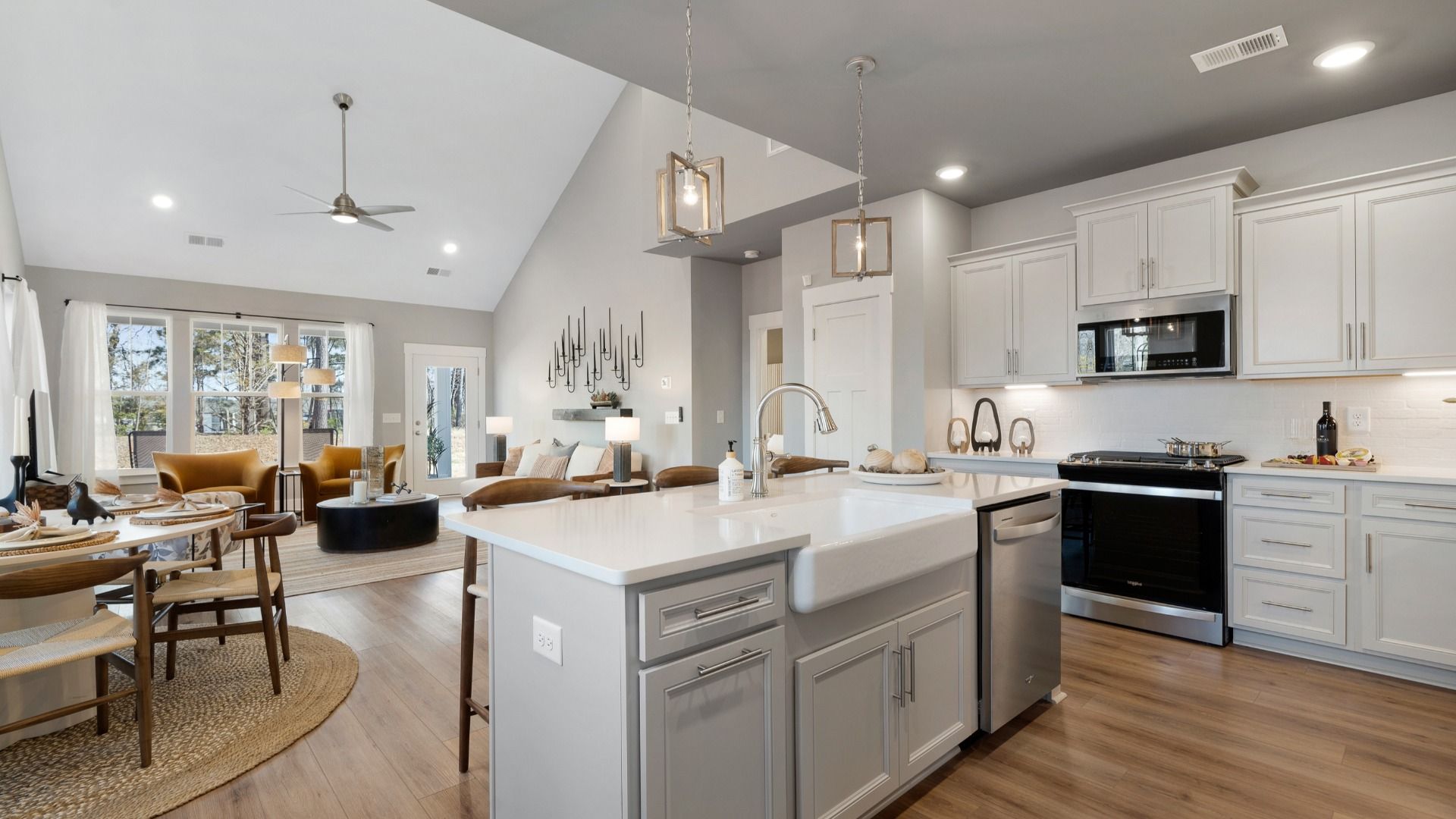 Lakehurst kitchen with white cabinetry, quartz countertops and a farmhouse sink in Anderson, SC:Open concept design with kitchen island overlooking the family room with two story ceilings at Village at Midway in Anderson
