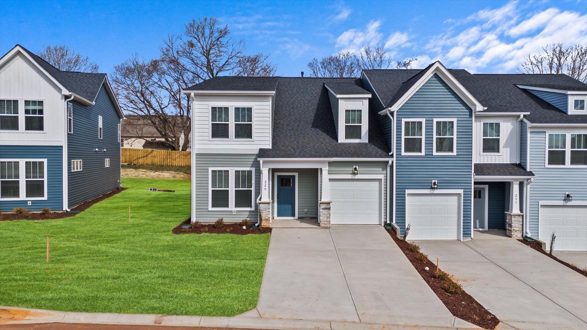 Townhome with craftsman exterior, blue and white vinyl siding and large windows in Lyman, SC:Townhome exterior with blue and white vinyl, stone columns, garage, and two car parking pad at Aspen Ridge by DRB Homes