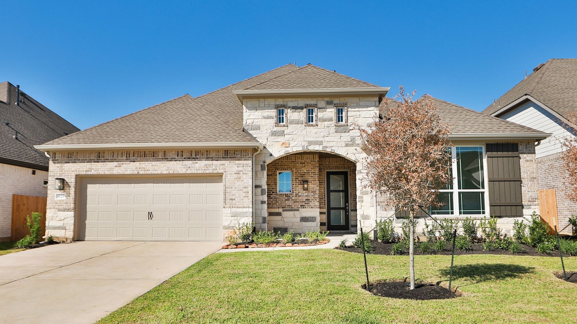 Yale House with Arched Entry and Stone Facade at Katy Lakes:Elegant stone and wood facade with arched entry and manicured landscaping in upscale Katy Lakes community.
