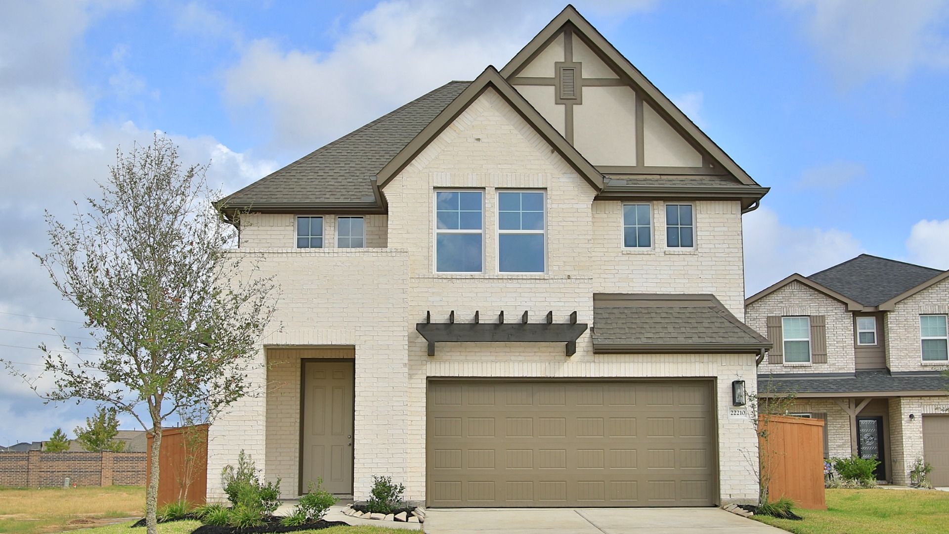 Two-Story Brick Home with Gabled Roof at Wayfinder, Cypress Green:Elegantly designed brick facade with gabled roof and wooden accents in Cypress Green. Luxurious, modern architecture.