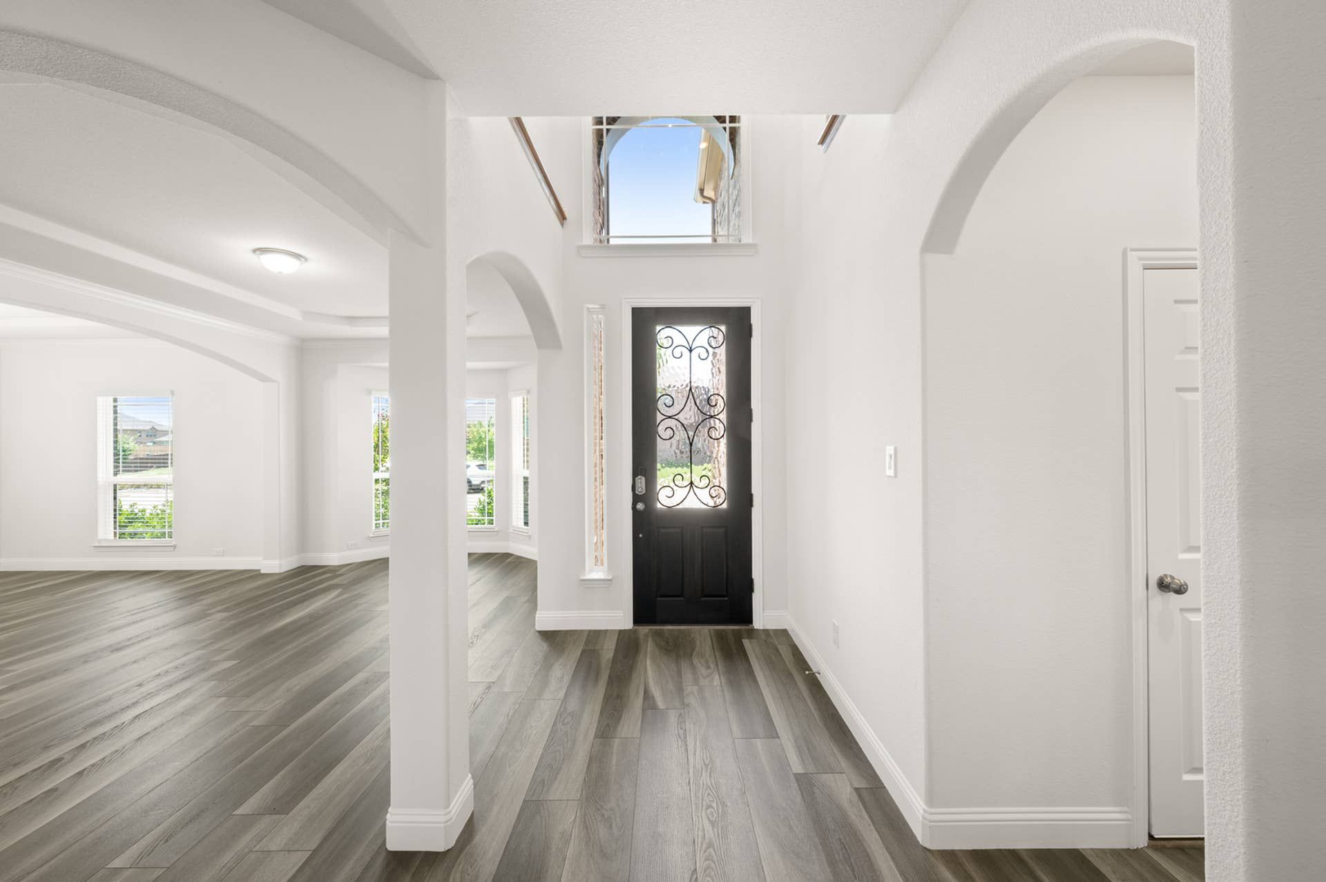 Interior Image:Bright entryway with arched openings, dark door, and wood flooring.
