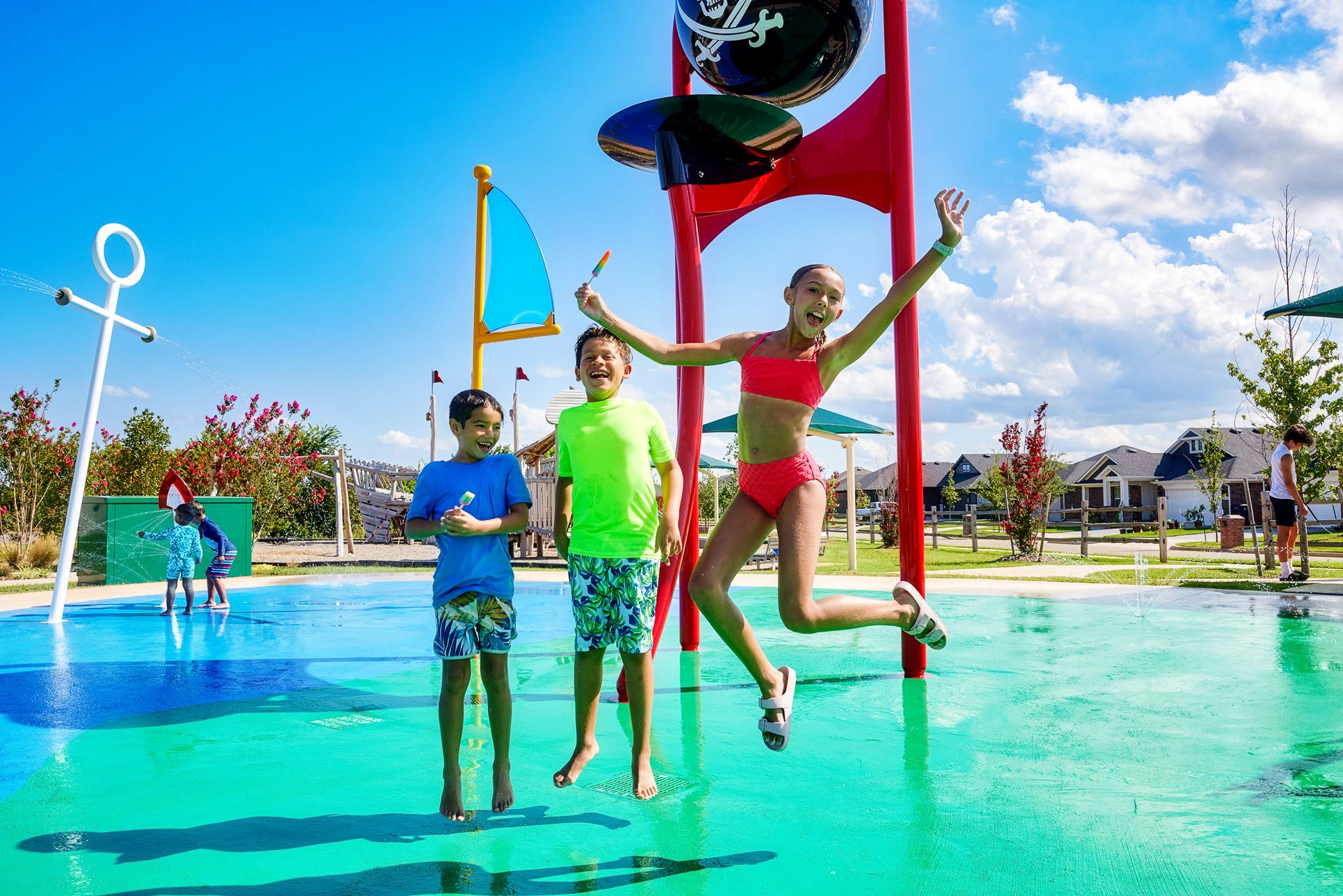 Girl and two boys enjoying popsicles at the pirate-themed splash pad in Abbot Lake neighborhood.:Kids at Pirate Splash Pad