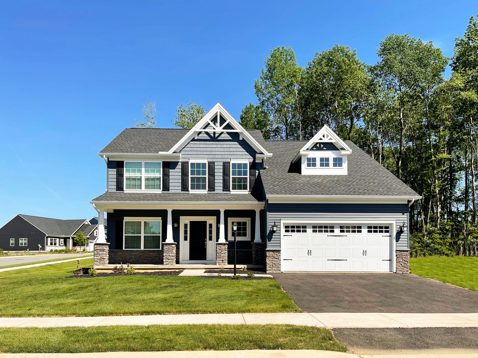 Two-story Craftsman-style home with dark blue siding, white trim, stone accents, and a double front gable.