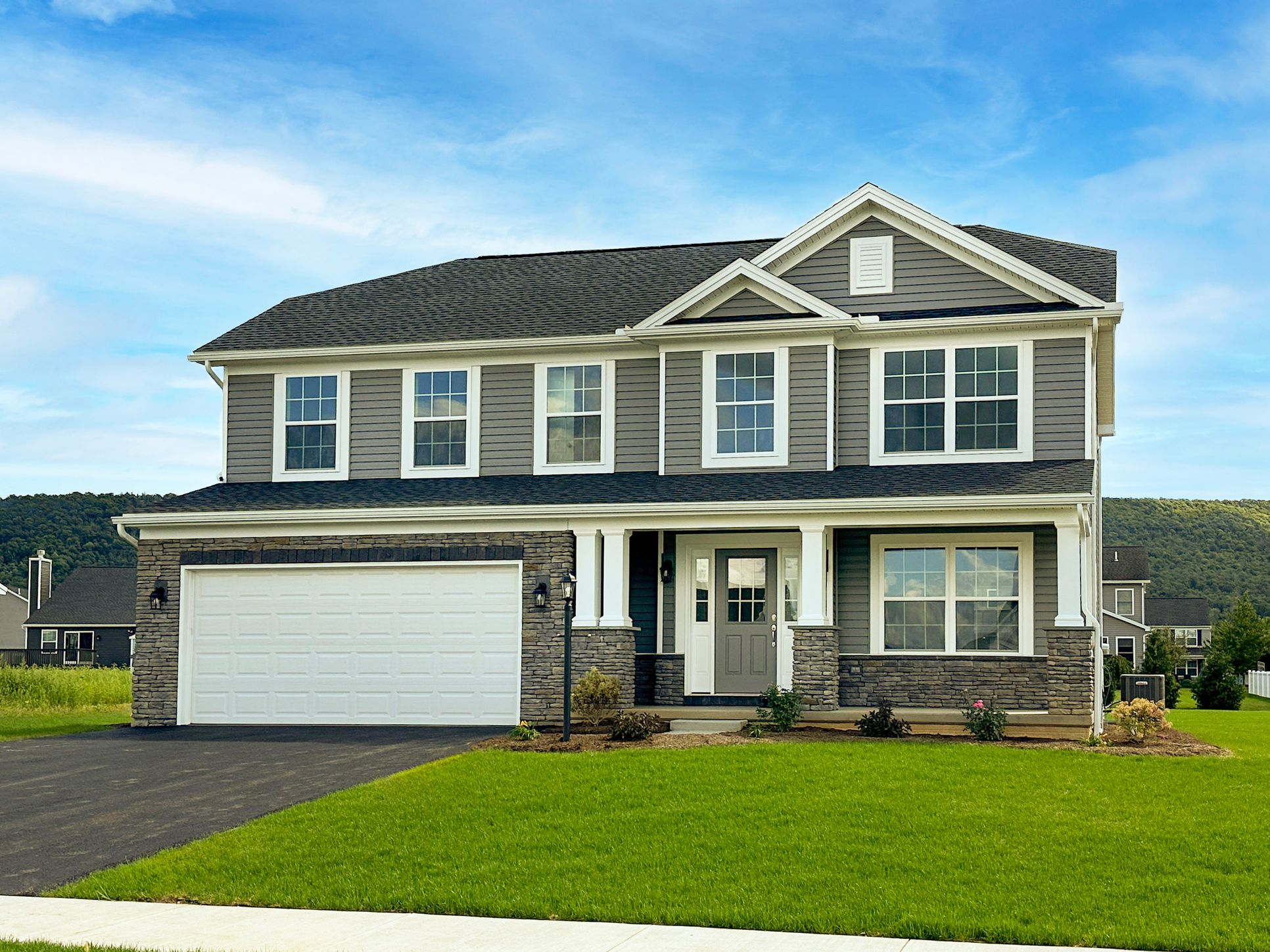Front view of a two-story home with gray siding, stone accents, white trim, and a double garage