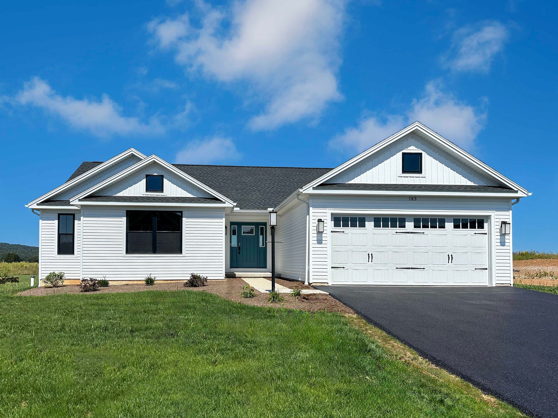 Front exterior of a white ranch-style home with a teal front door, two-car garage, landscaped yard, and paved driveway.
