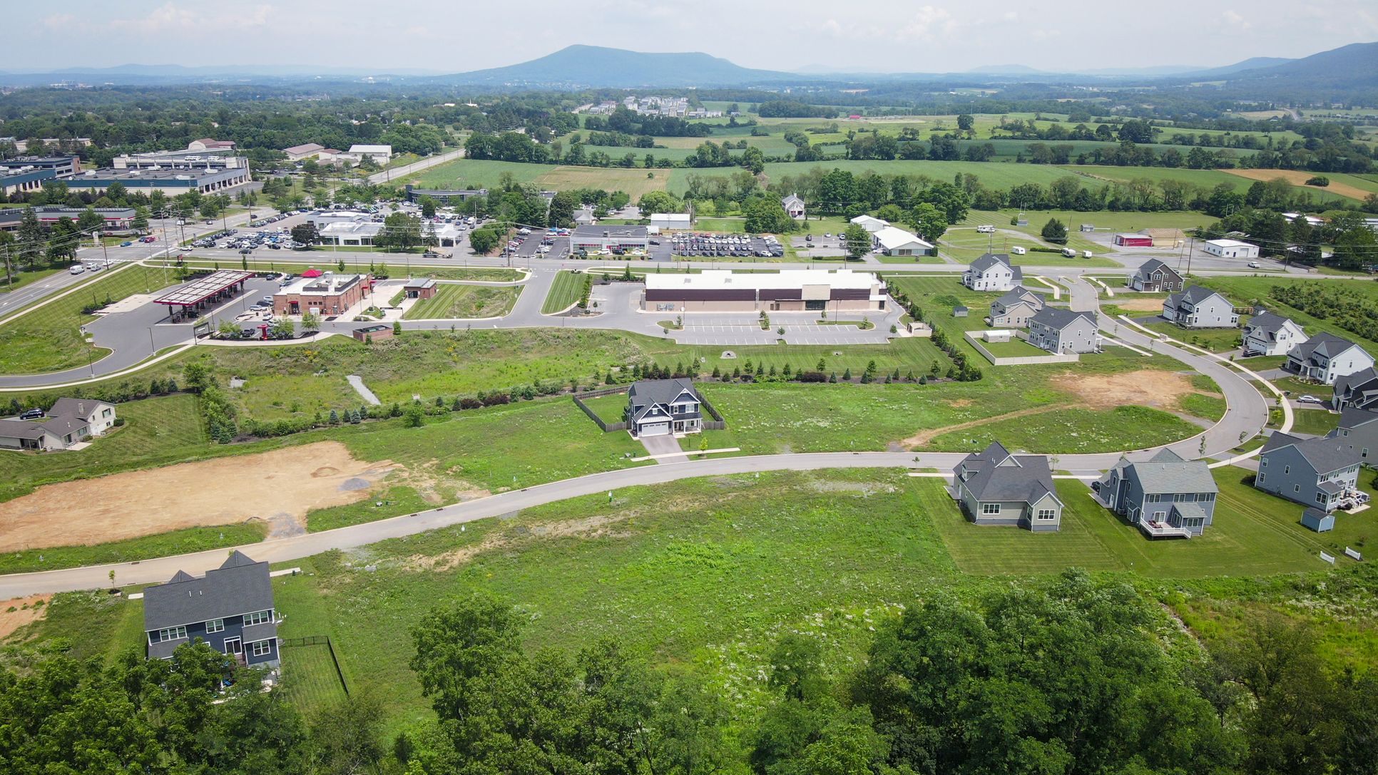 Drone view of Orchard View community near shops and farmland with mountain backdrop
